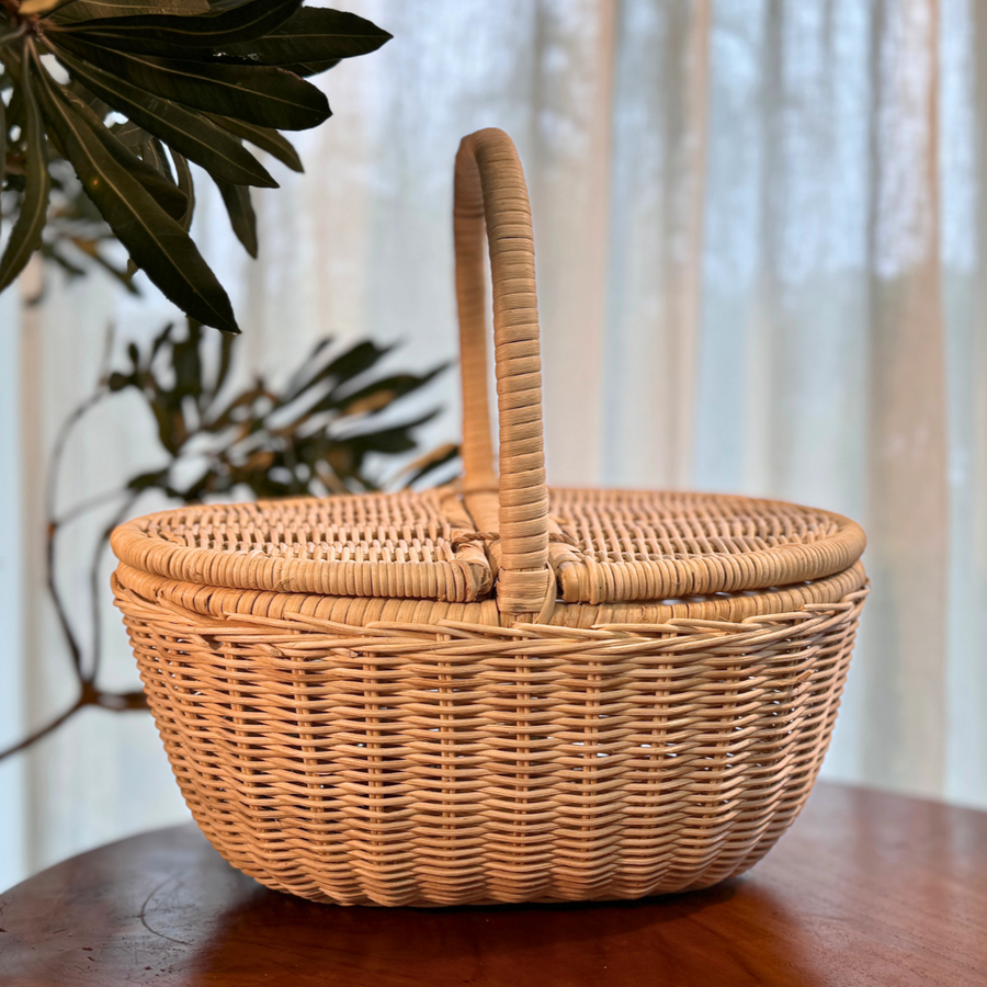 Wicker picnic basket on a wooden table with plants in the background